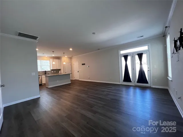 an empty room with wooden floor and kitchen view