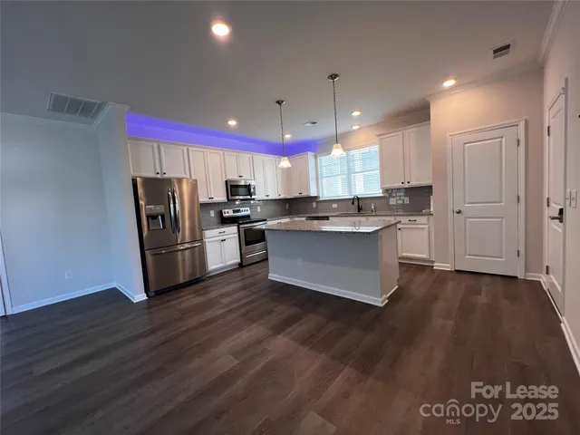 a kitchen with stainless steel appliances granite countertop a refrigerator a sink dishwasher a stove and a microwave oven on the wooden floor