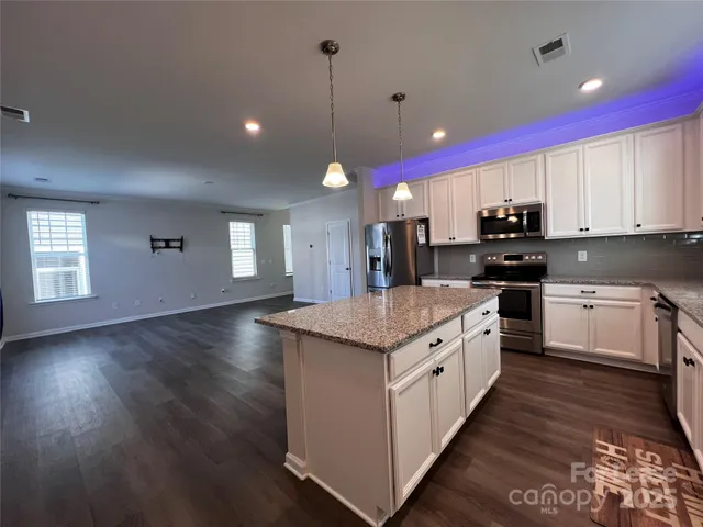 a large kitchen with granite countertop a stove a sink dishwasher a microwave oven and a dining table with wooden floor