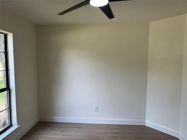 an empty room with wooden floor ceiling fan and windows
