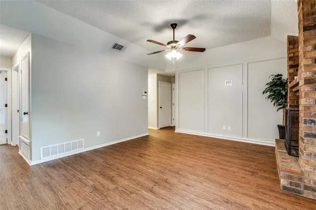 a view of an empty room with wooden floor and a ceiling fan