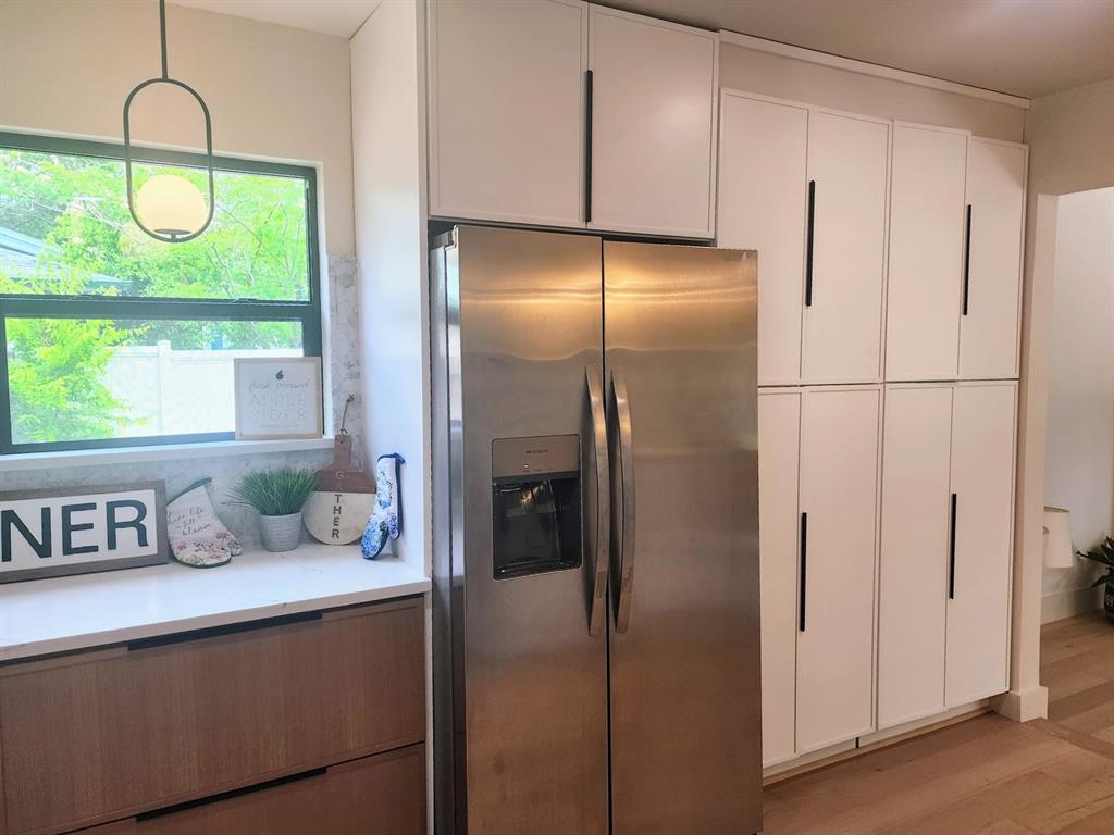 2908 Washington Street Commerce, TX 75428 - Photo 6 of 29 Modern kitchen featuring extensive white cabinetry with matte black hardware, a stainless steel side-by-side refrigerator, and stone countertops