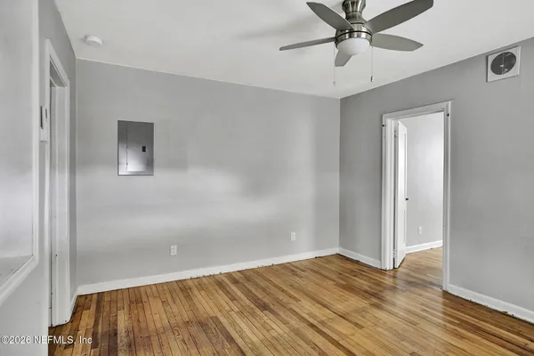 a view of an empty room with wooden floor and a ceiling fan