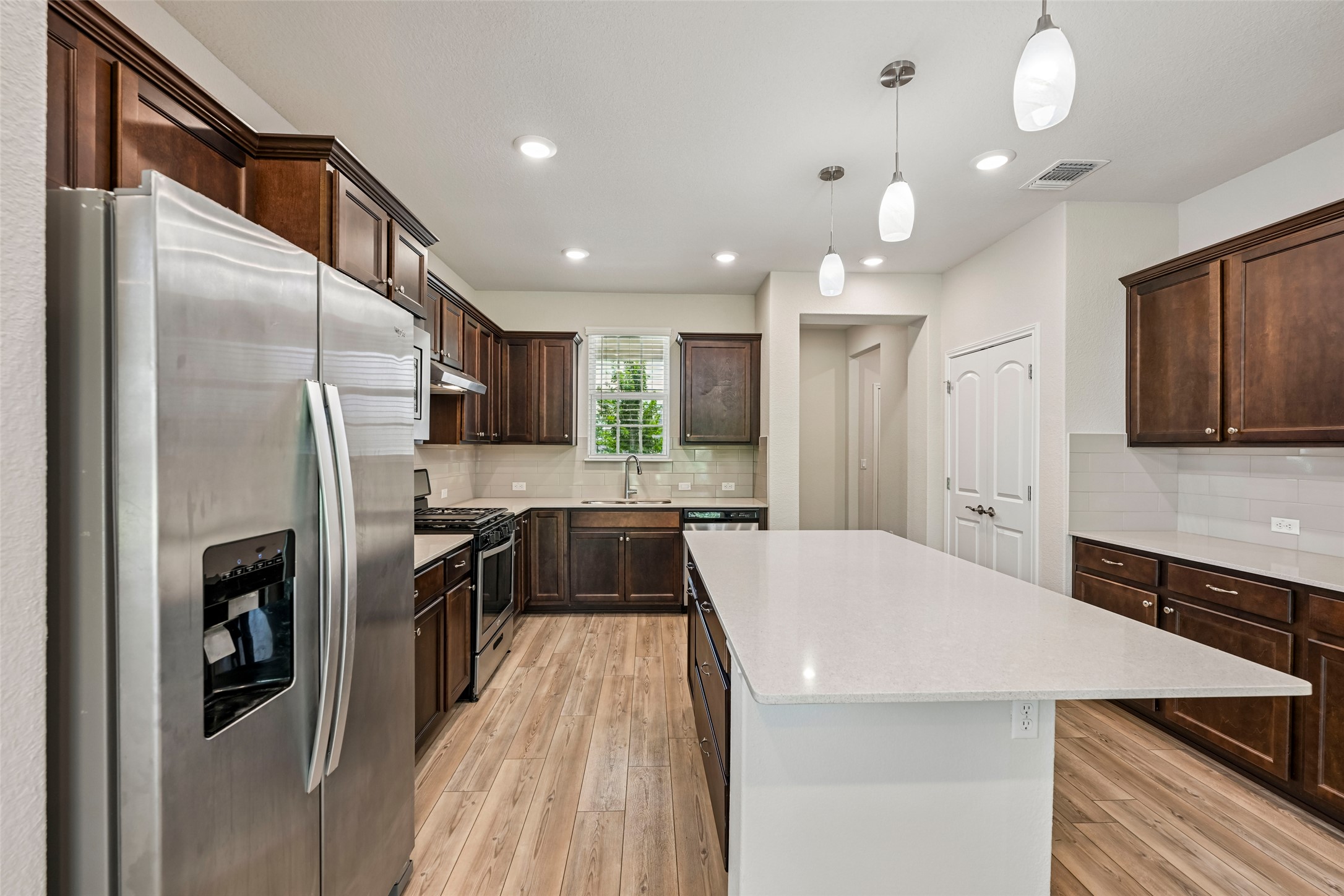401 Yorktown Street Georgetown, TX 78633 - Photo 9 of 38 Kitchen featuring an expansive center island with a light-toned countertop, wood-finish flooring, dark wood cabinetry, stainless steel appliances, and pendant lighting