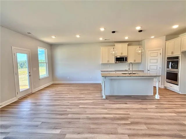 a view of kitchen with kitchen island granite countertop a stove top oven a sink and white cabinets