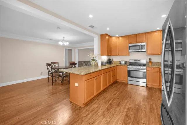 a kitchen with stainless steel appliances granite countertop wooden cabinets a sink a stove a dining table and chairs