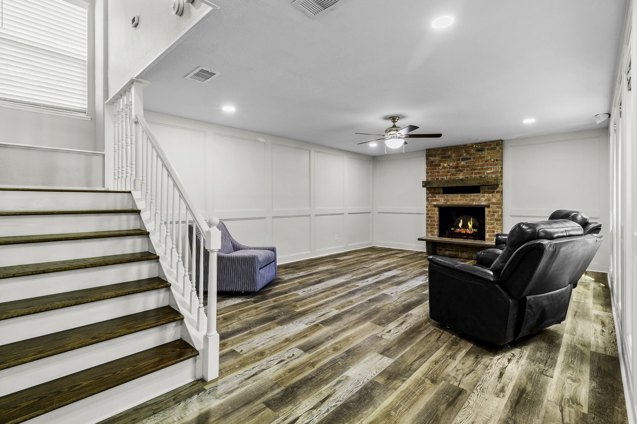 21 Red Oak Circle Point Blank, TX 77364 - Photo 3 of 32 This inviting living room features a cozy brick fireplace, wood flooring, and a ceiling fan. It has a modern staircase with white railing and ample natural light. Comfortable seating completes the welcoming atmosphere.