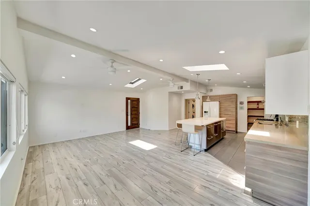 a large white kitchen with kitchen island a stove a refrigerator a sink dishwasher with a dining table and chairs with wooden floor