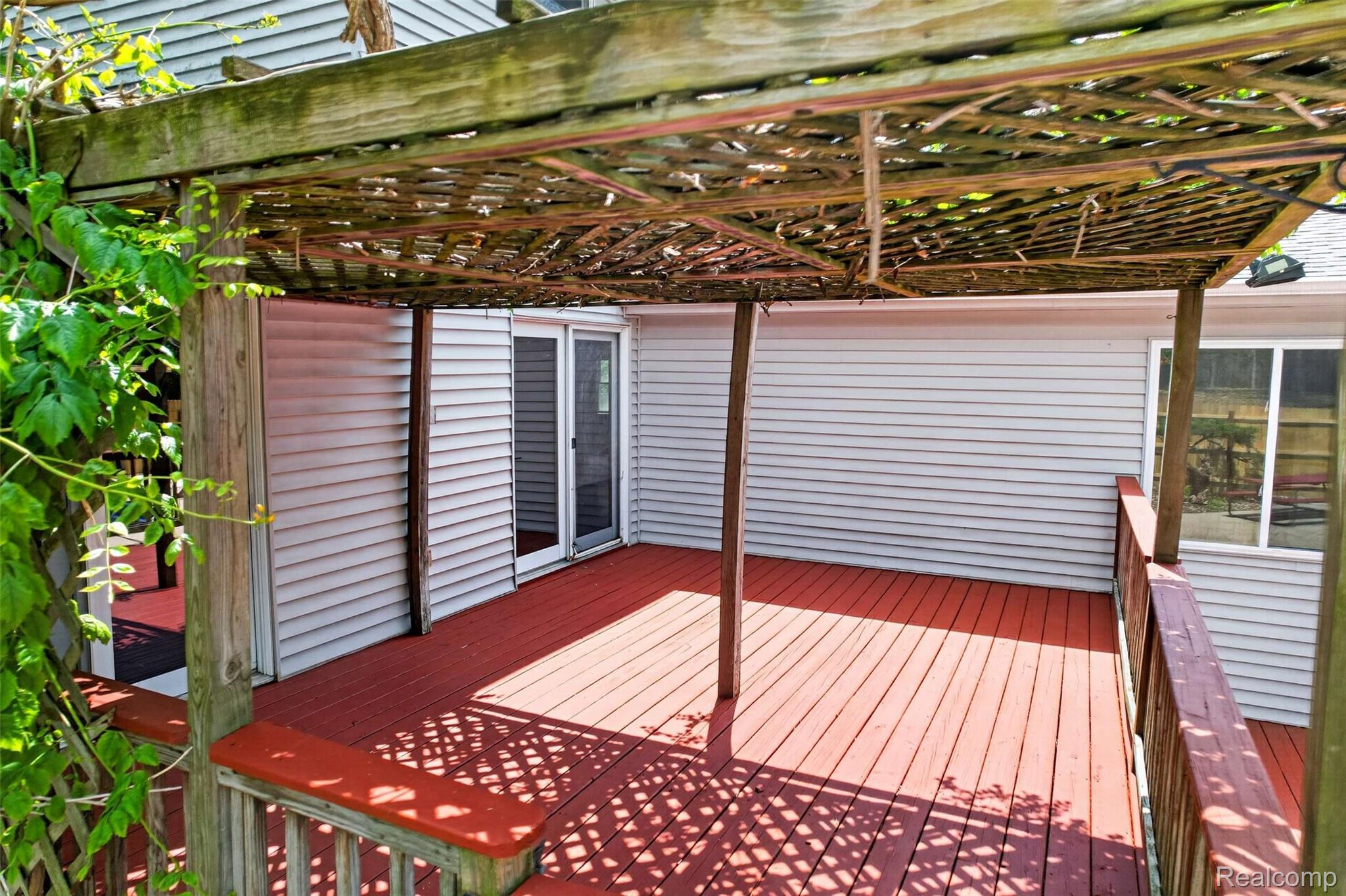 1437 East Cook Road Grand Blanc, MI 48439 - Photo 16 of 69 Spacious outdoor deck featuring red-stained wood flooring and railing, a wood pergola, and direct access to the interior via a sliding glass door