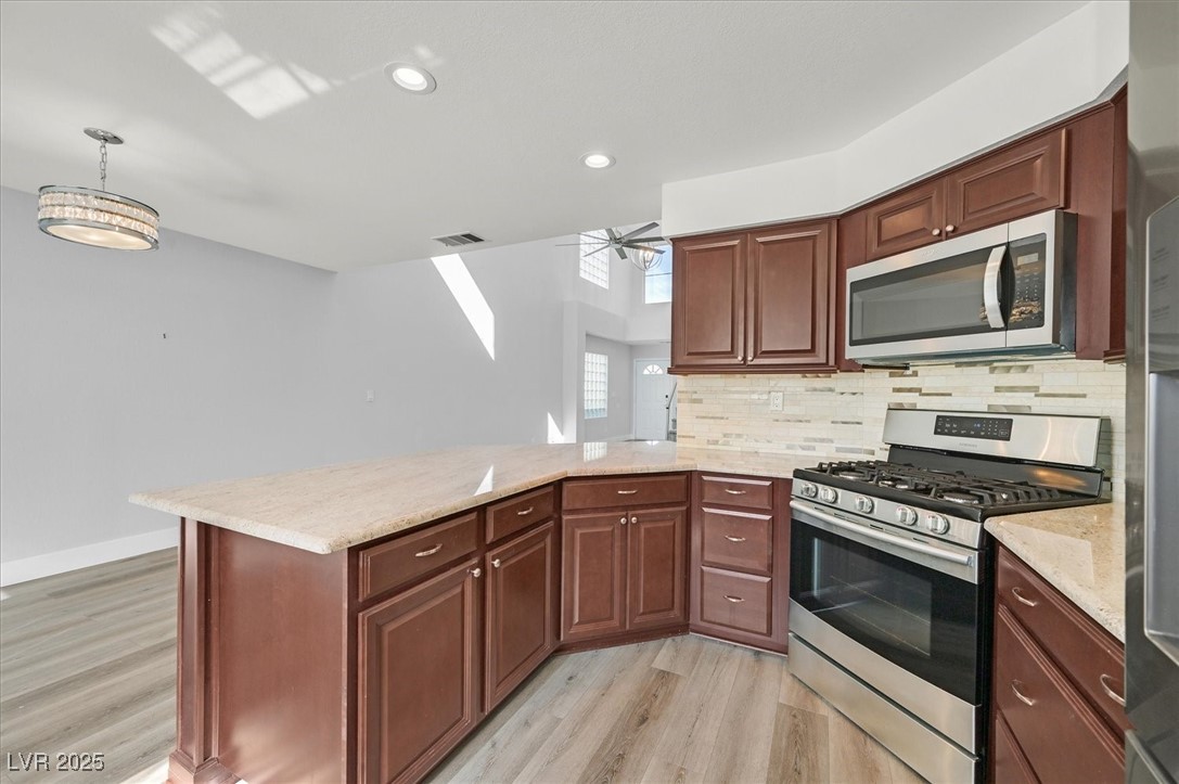 5421 Painted Mirage Road Las Vegas, NV 89149 - Photo 10 of 35 Kitchen featuring stainless steel appliances, a peninsula, visible vents, hanging light fixtures, and backsplash