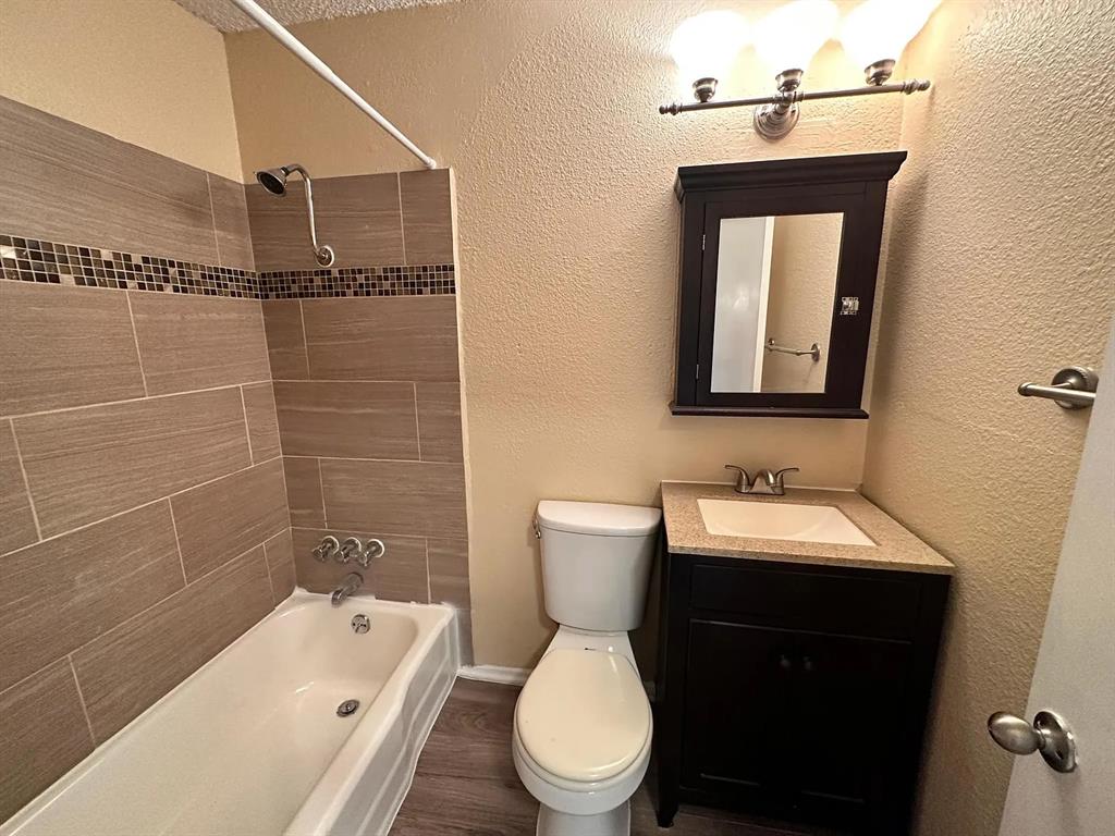 2401 Manor Road, Unit 220 Austin, TX 78722 - Photo 2 of 17 Tiled walls frame the tub shower next to a dark wood vanity with stone counters.