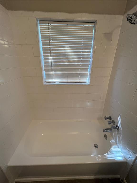 1622 Centerville Road Dallas, TX 75228 - Photo 13 of 19 White tiled shower enclosure with a window, white bathtub, and chrome fixtures