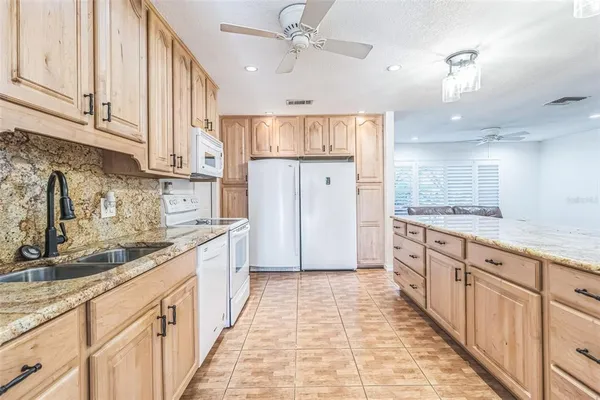 a large kitchen with stainless steel appliances kitchen island granite countertop a refrigerator a sink dishwasher and white cabinets with wooden floor