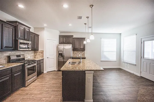 a large kitchen with stainless steel appliances kitchen island granite countertop a stove a sink a refrigerator and white cabinets with wooden floor