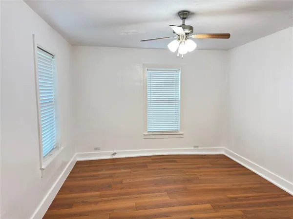 an empty room with wooden floor chandelier fan and windows