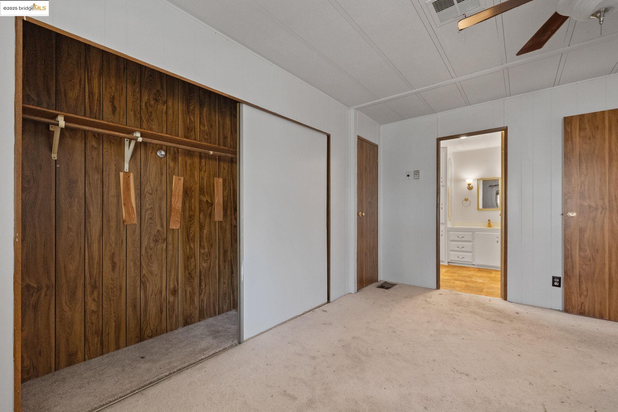 10956 Green Street, Unit 186 Columbia, CA 95310 - Photo 11 of 21 Unfurnished bedroom with a closet, carpet flooring, a ceiling fan, connected bathroom, and wooden walls
