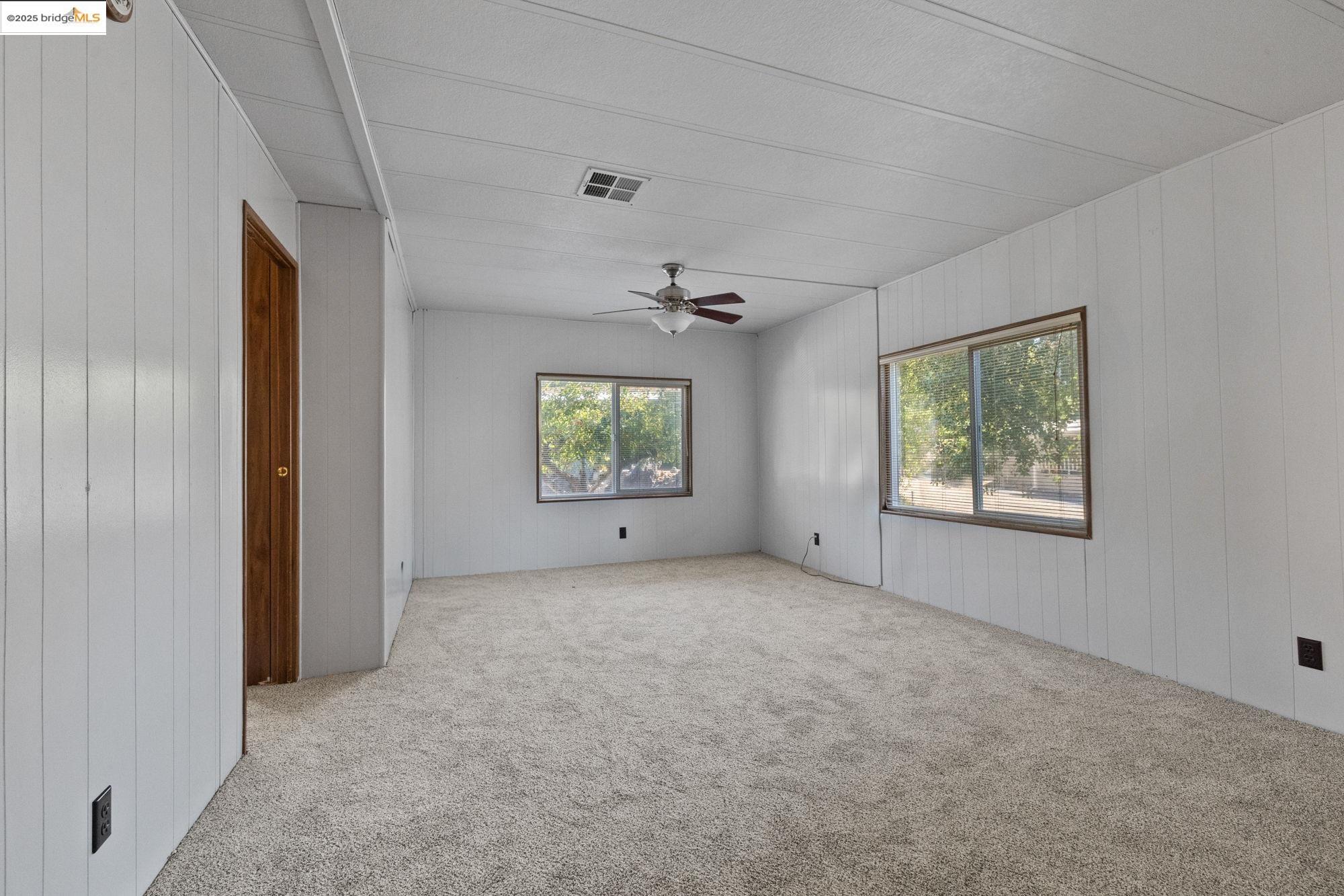 10956 Green Street, Unit 186 Columbia, CA 95310 - Photo 16 of 21 Unfurnished room with plenty of natural light, carpet floors, wooden walls, and a ceiling fan