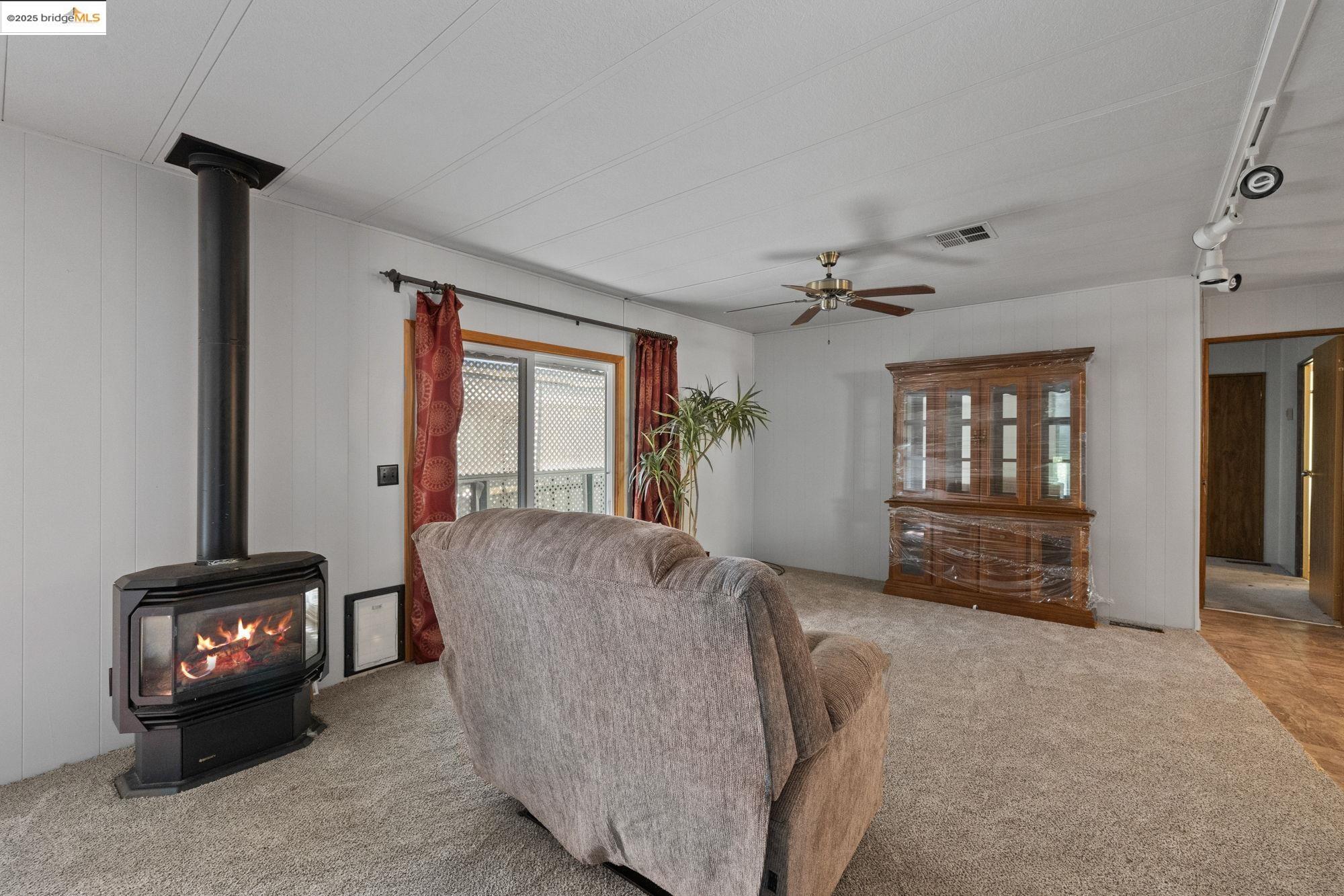 10956 Green Street, Unit 186 Columbia, CA 95310 - Photo 3 of 21 Living area featuring a wood stove, carpet, a ceiling fan, and wood walls