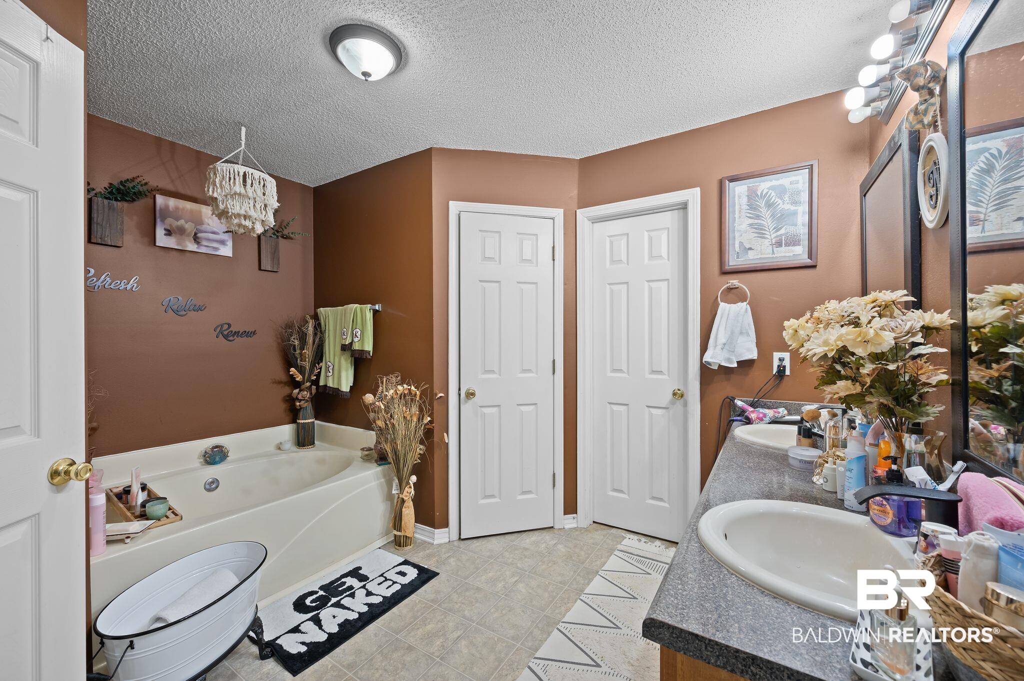 52923 Ammons Road Perdido, AL 36562 - Photo 22 of 35 Bathroom with double vanity, a chandelier, a bath, tile patterned flooring, and a textured ceiling