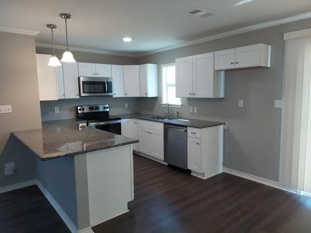 a kitchen with stainless steel appliances granite countertop a sink a stove top oven a refrigerator a sink and dishwasher with wooden floor