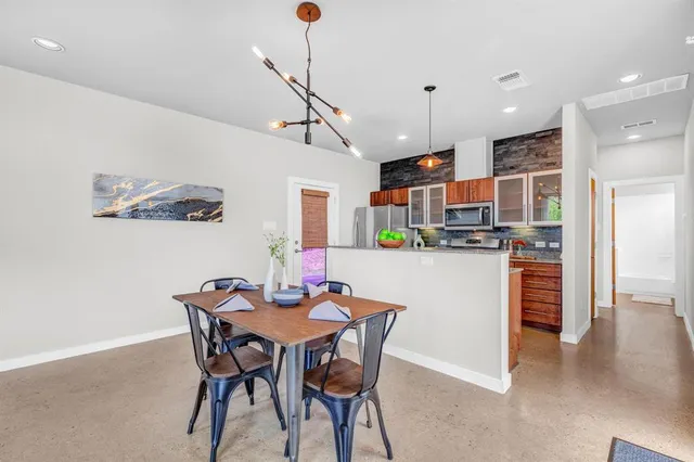 a kitchen with stainless steel appliances kitchen island granite countertop a dining table chairs and a refrigerator