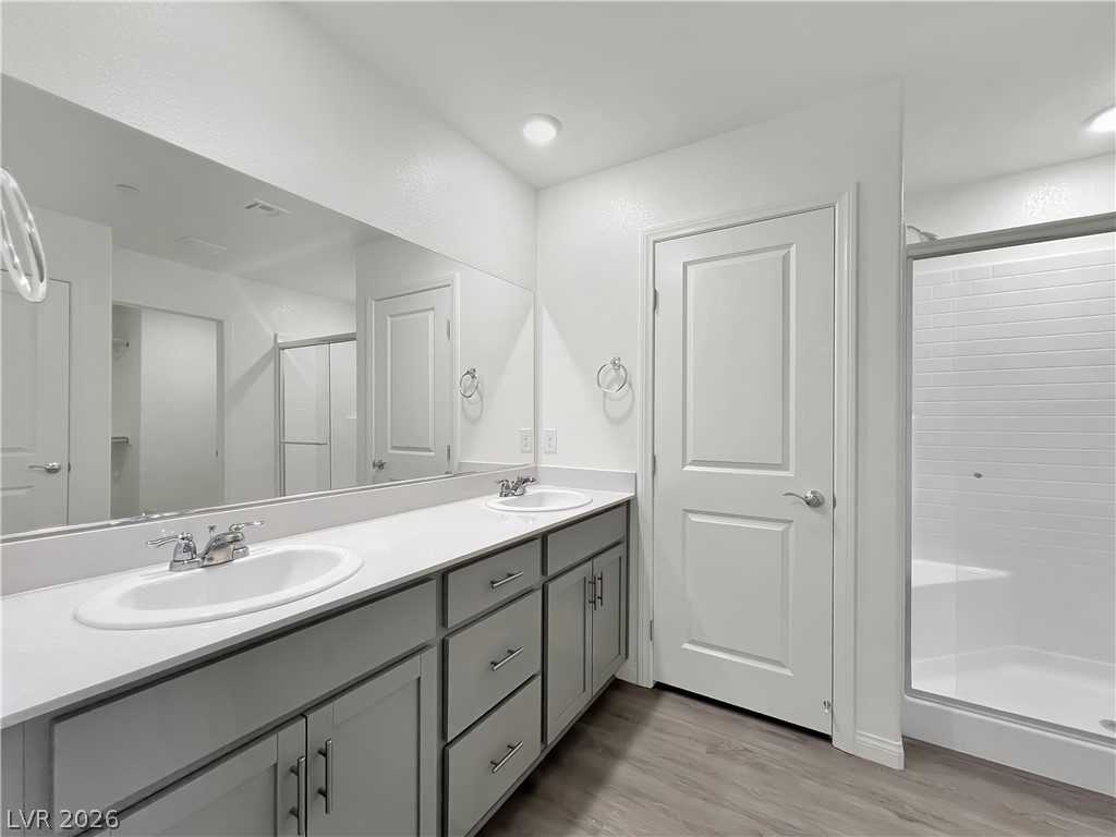 9984 Indigo Cliffs Street Las Vegas, NV 89141 - Photo 16 of 31 Bathroom featuring a sink, wood finished floors, a stall shower, and double vanity
