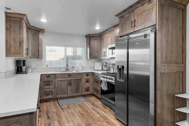 1426 South 1450th Street West Mapleton, UT 84664 - Photo 33 of 50 Kitchen featuring wood-finish cabinetry, stainless steel appliances, a white solid surface countertop, and wood-finish flooring