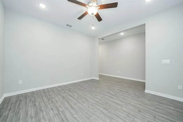 a view of an empty room with wooden floor and a ceiling fan