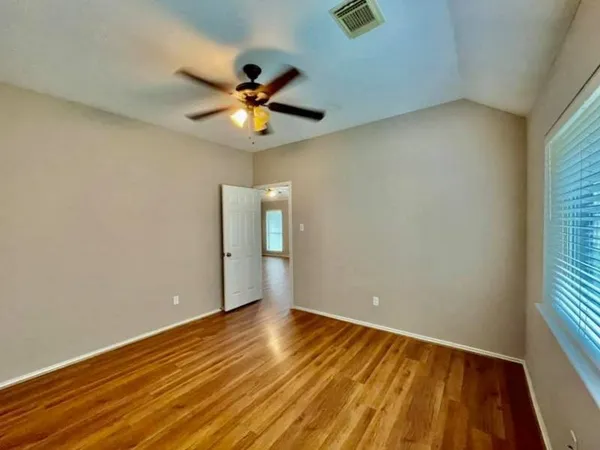 an empty room with wooden floor fan and windows