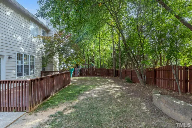 a view of a backyard with large trees and wooden fence