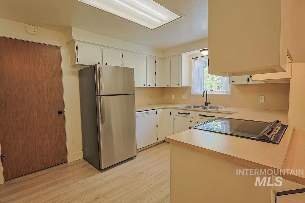 640 Morrison Street Twin Falls, ID 83301 - Photo 7 of 30 Kitchen featuring wood-finish flooring, white cabinetry with dark hardware, stainless steel refrigerator, built-in cooktop, and a double basin sink with a gooseneck faucet