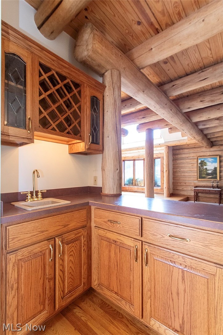 1871 Mattingly Road Hinckley, OH 44233 - Photo 15 of 50 Indoor wet bar with rustic walls, glass insert cabinets, light wood-style flooring, wood finish cabinetry, and a wood ceiling with exposed beams