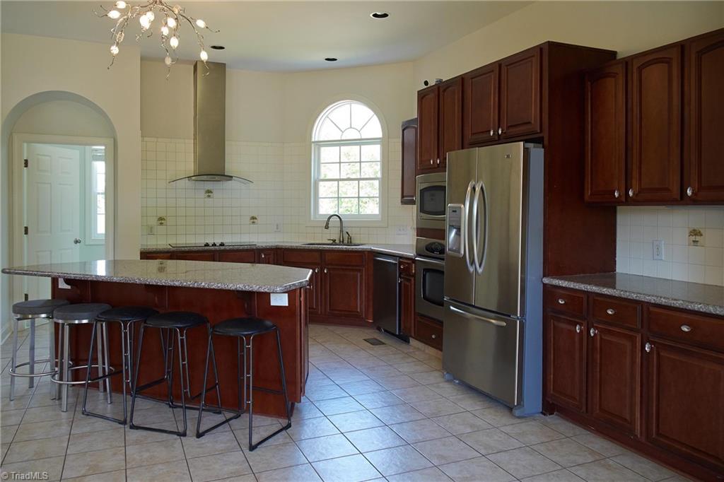 602 Bobcat Road Summerfield, NC 27358 - Photo 8 of 30 Kitchen has tile floors, stainless appliances, granite counters, tile back splash, and a large island. Door on the left leads into a huge laundry room.