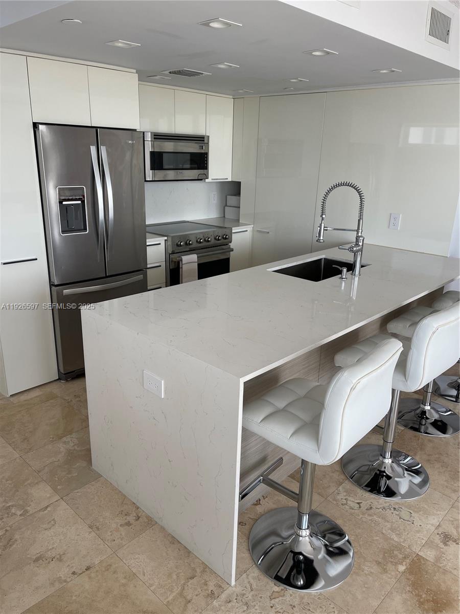 8911 Collins Avenue, Unit 1201 Surfside, FL 33154 - Photo 5 of 27 a kitchen with refrigerator and chairs