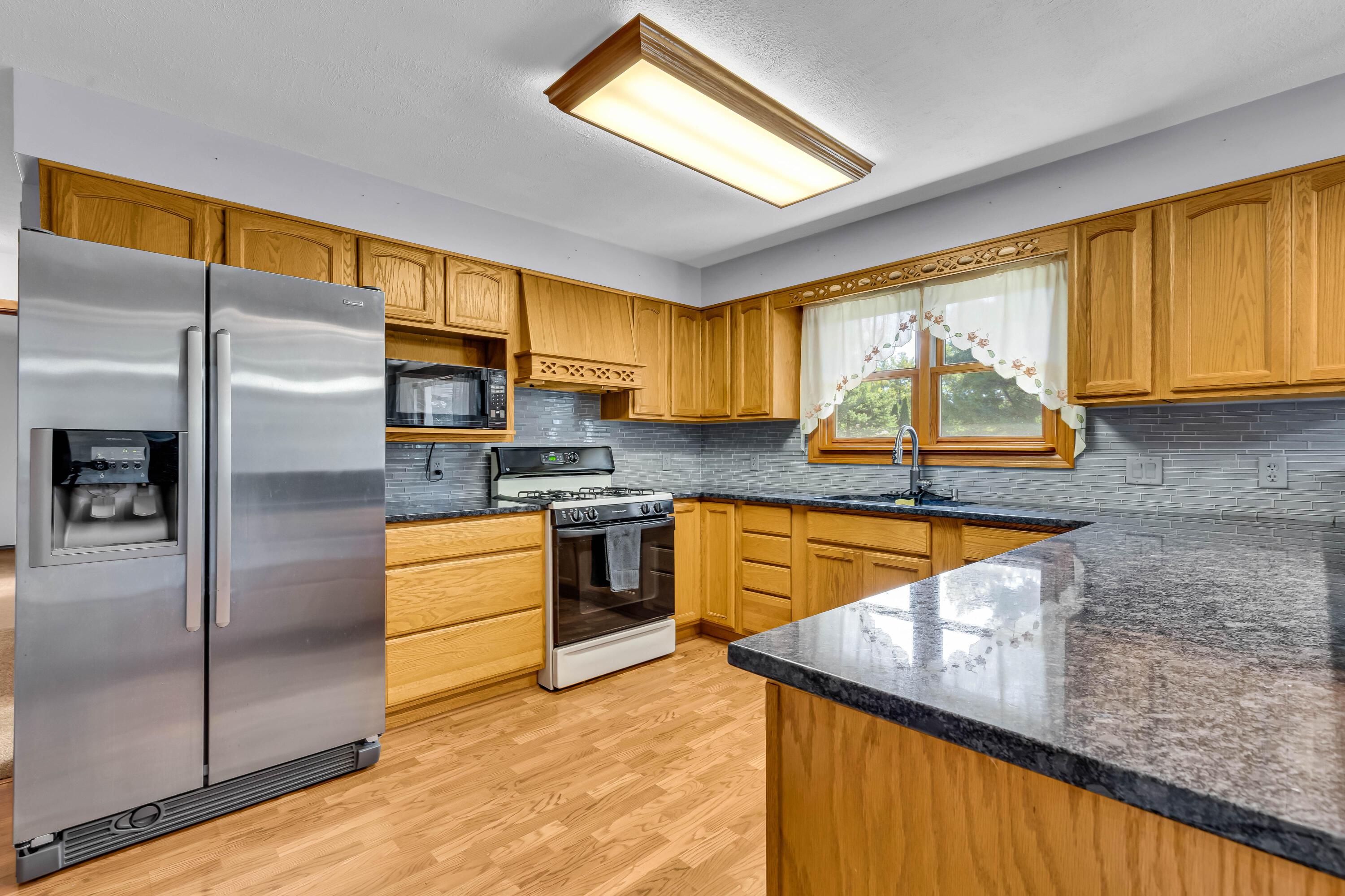 1213 East Cooke Road Columbus, OH 43224 - Photo 20 of 57 • Laminate flooring • Tan painted walls • Oak cabinets • New granite countertops ~ 2020 • Breakfast bar ledge • Track lighting • Kenmore® refrigerator • Tappan® microwave • General Electric® gas stove • New General Electric dishwasher ~ 2020 • Insinkerator® disposal • Glass tile backsplash • Single bowl, stainless steel sink with soap dispenser • Ceiling light • Pantry closet