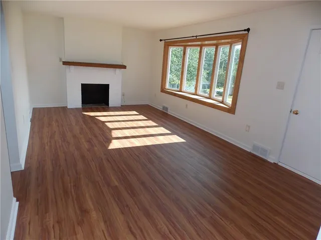 a view of an empty room with wooden floor fireplace and a window