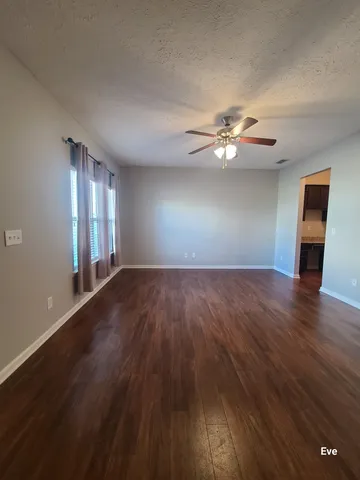 a view of an empty room with wooden floor and a ceiling fan