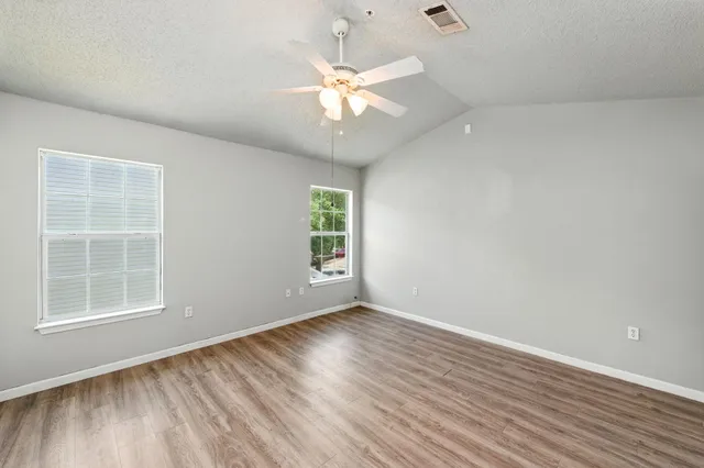an empty room with wooden floor chandelier fan and windows
