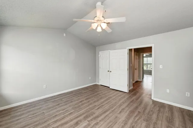 a view of an empty room with wooden floor and a ceiling fan