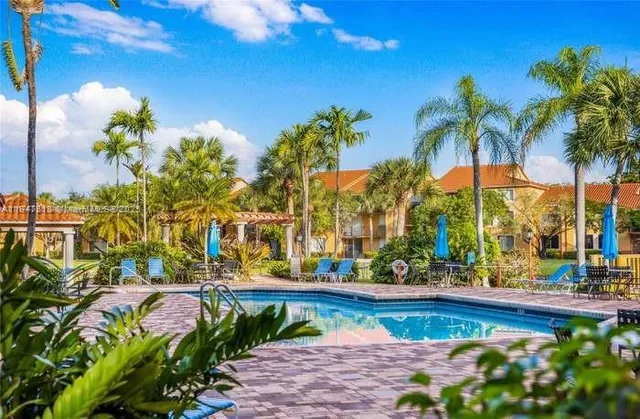 a view of swimming pool with a lawn chairs under palm trees