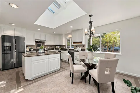 a kitchen with stainless steel appliances granite countertop a dining table chairs refrigerator microwave and cabinets