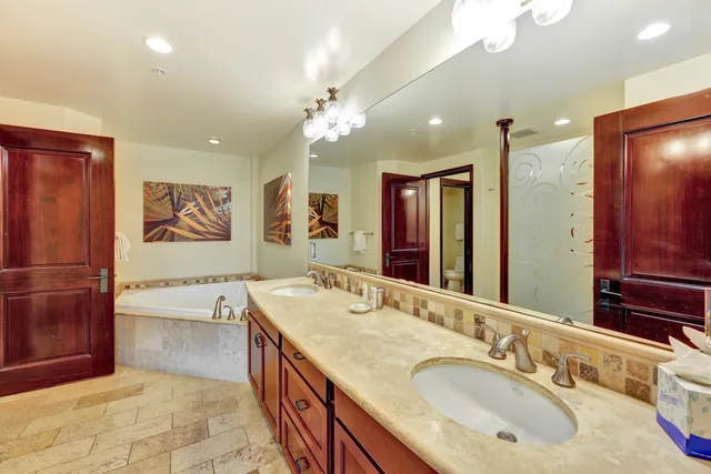 a spacious bathroom with a granite countertop double vanity sink a mirror and a bathtub
