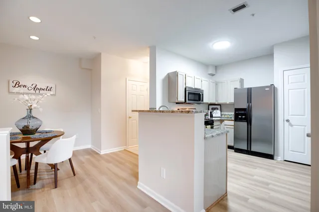 a kitchen with stainless steel appliances a refrigerator a stove top oven a sink dishwasher a dining table and chairs with wooden floor