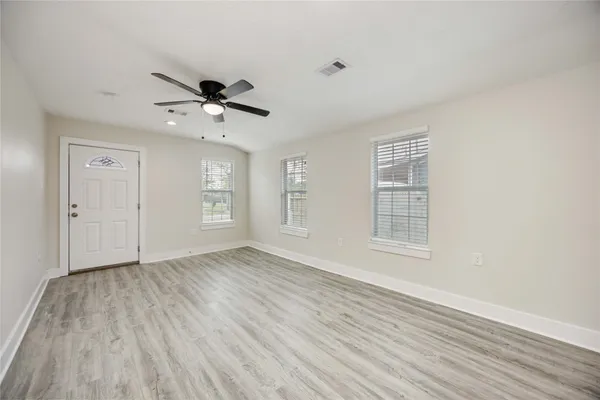 an empty room with wooden floor ceiling fan and windows