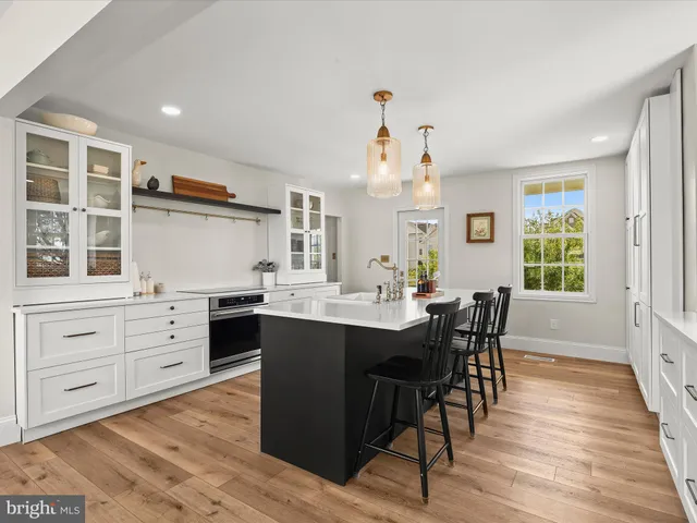 a large white kitchen with granite countertop a stove oven a sink dishwasher and white cabinets with wooden floor