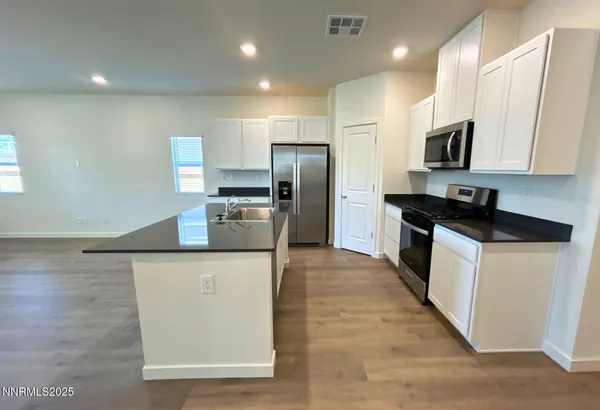 a kitchen with stainless steel appliances granite countertop a stove a sink a refrigerator and white cabinets with wooden floor