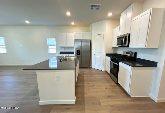 a kitchen with stainless steel appliances granite countertop a stove a sink a refrigerator and white cabinets with wooden floor