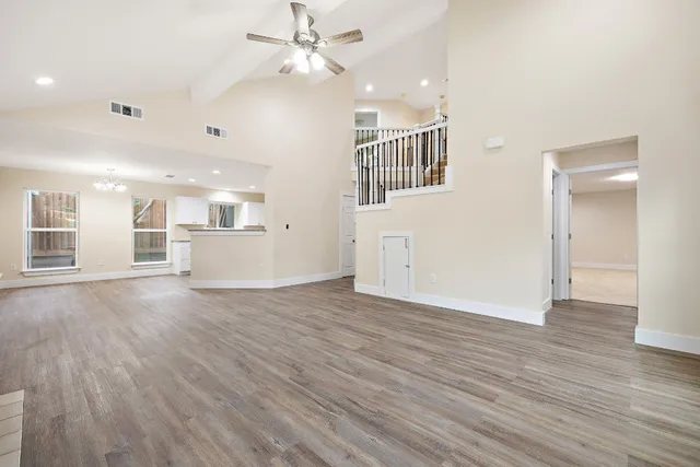 a view of an empty room with wooden floor and a ceiling fan