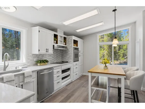a kitchen with stainless steel appliances granite countertop a stove a sink dishwasher and white cabinets with wooden floor