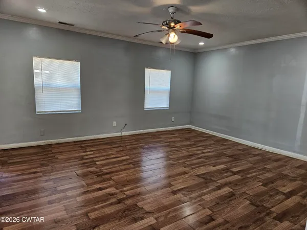 an empty room with wooden floor chandelier fan and windows